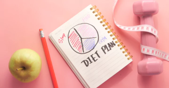 notebook written on it "diet plan" along with an apple, pen and weight bell
